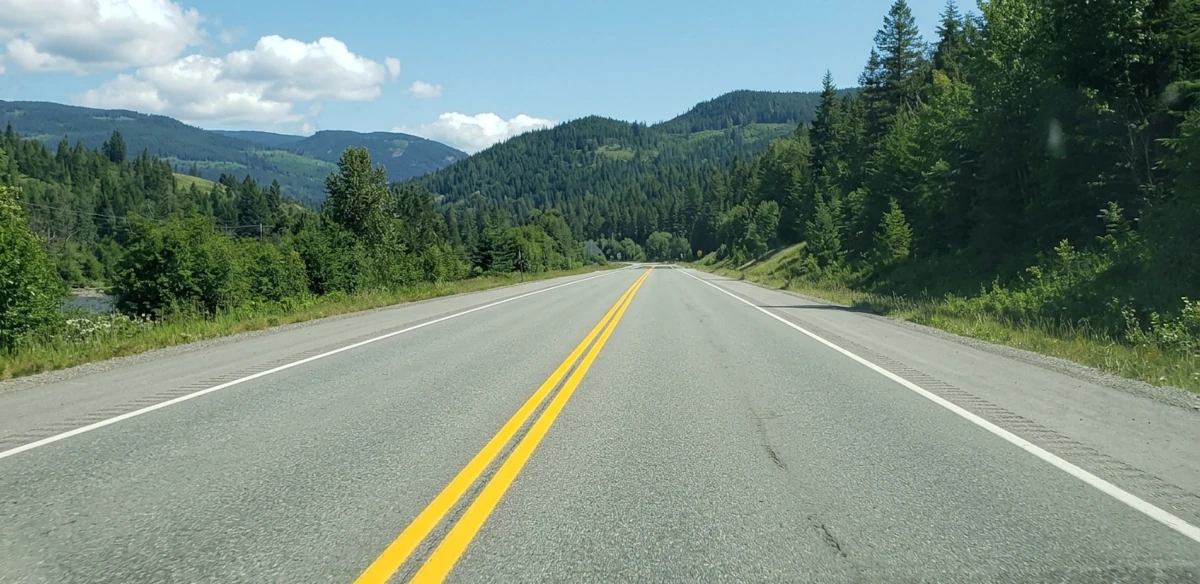 A driver's view of a two-lane British Columbia highway with a distinct double solid yellow line down the center